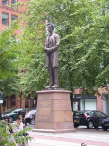 Bronze statue of Abraham Lincoln. He is standing on a pedestal surrounded by trees. 